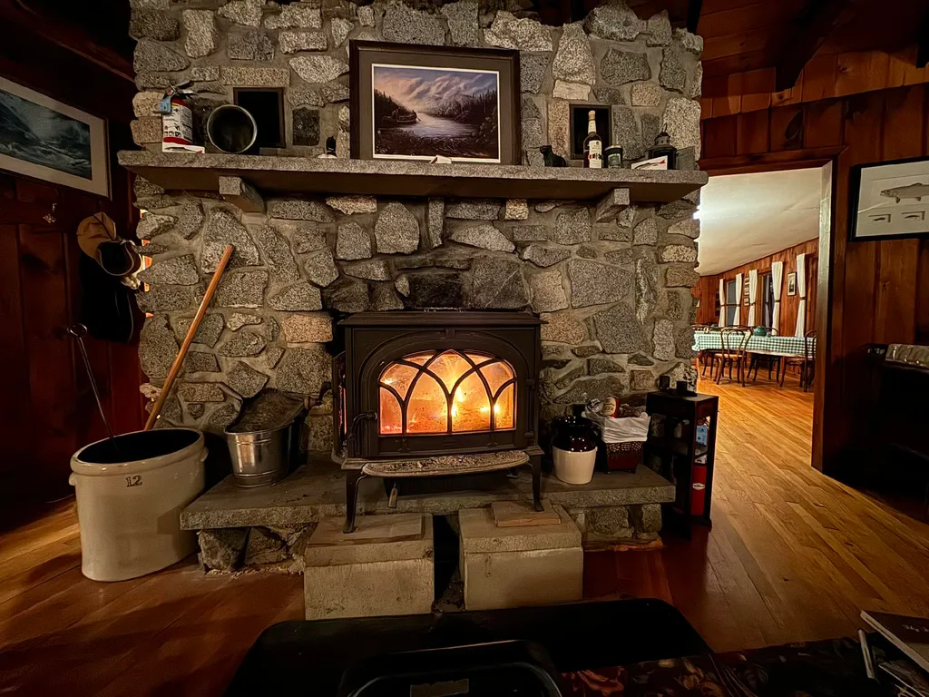 A cozy living room with a stone fireplace, a lit fire, and a wooden floor.