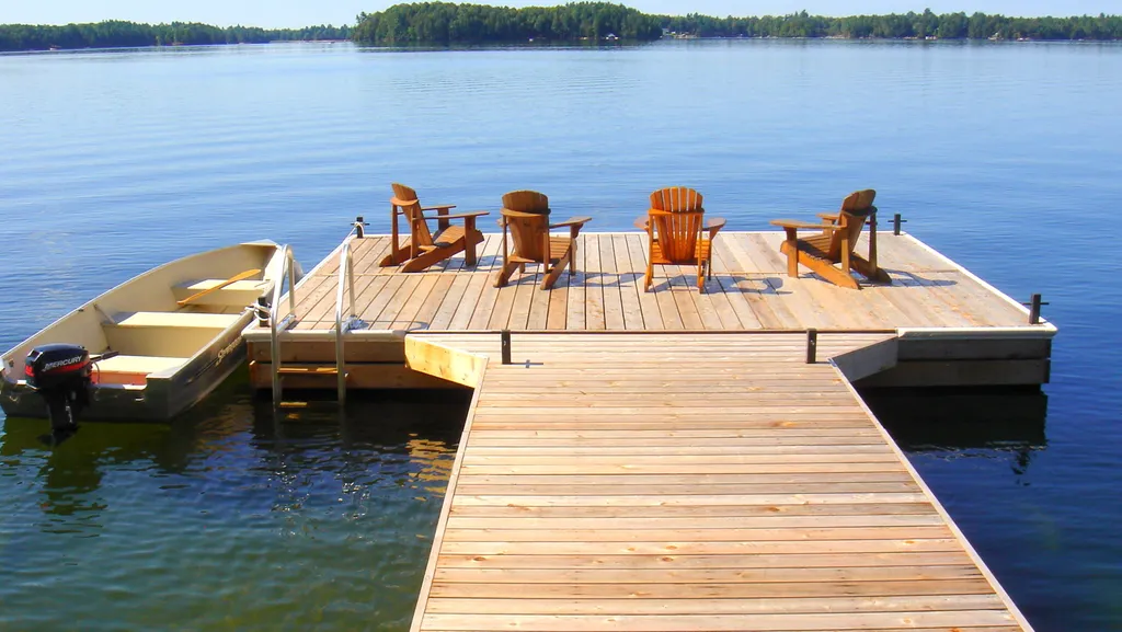 A wooden dock with four chairs and a small boat on the water.