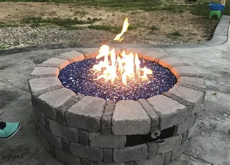 A round fire pit with burning blue glass and a stone border.
